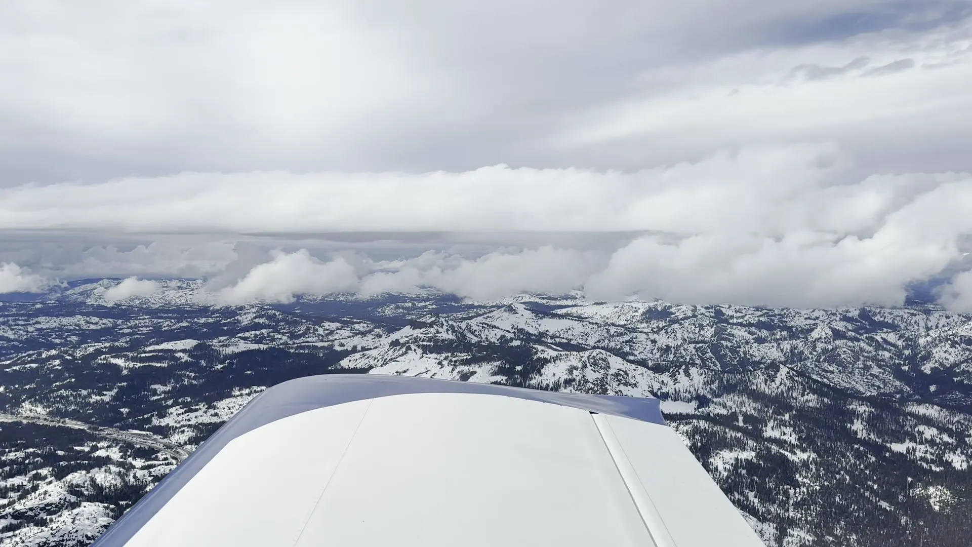 Snow-capped mountains and clouds seen from a small plane's wing
